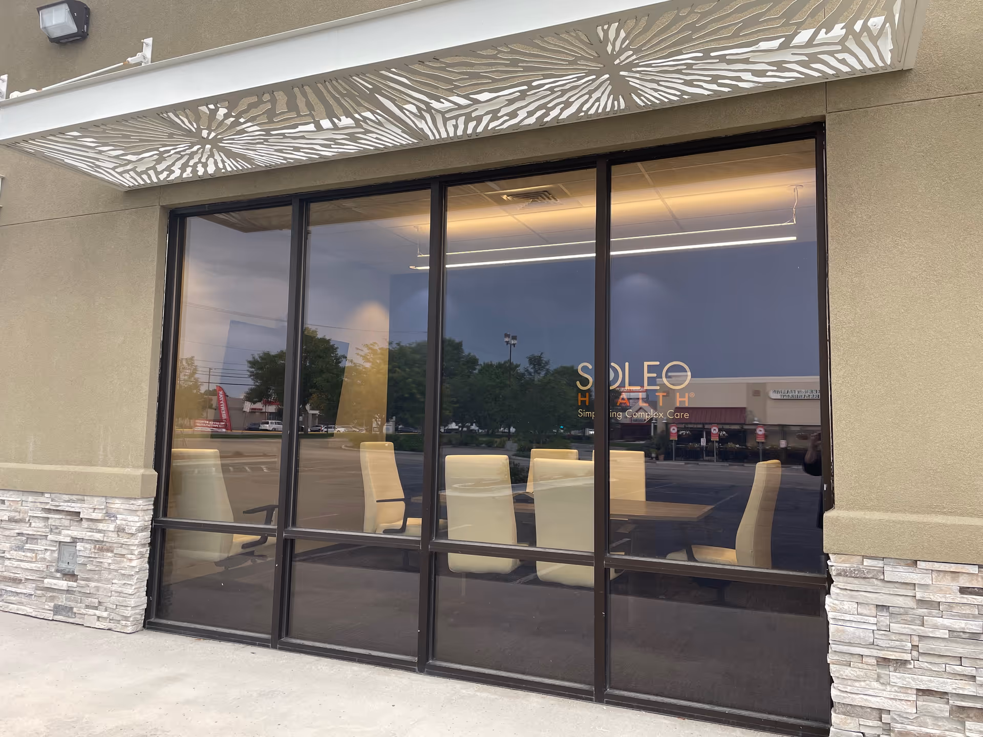 Front exterior of Soleo Health facility with large glass windows, beige walls, and interior chairs visible.