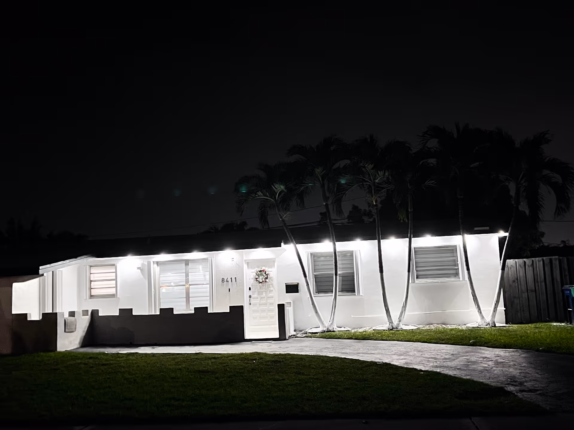 Night exterior of a single-story white facility with palm trees and illuminated entrance.