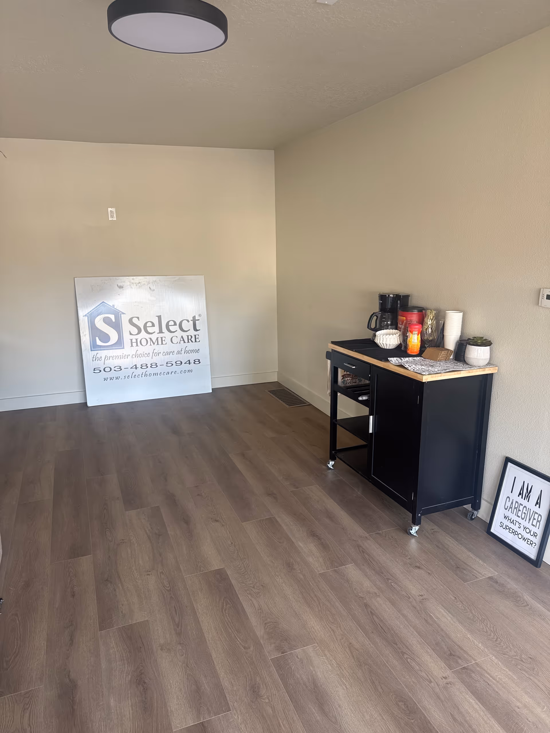 An empty room with wood-like flooring, a beverage cart, and a Select Home Care sign.