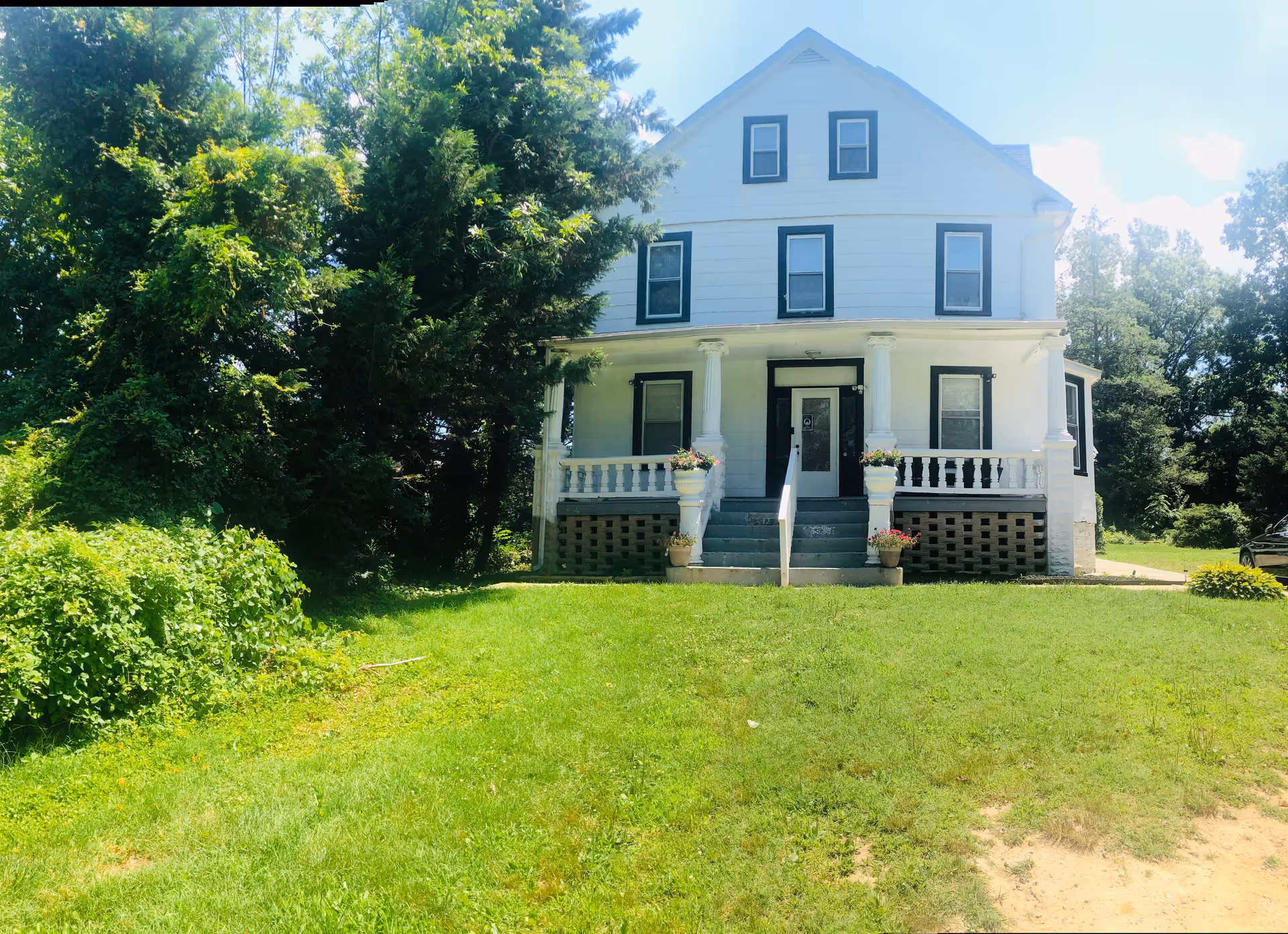 White two-story house with a front porch, columns, and surrounding greenery in the yard.