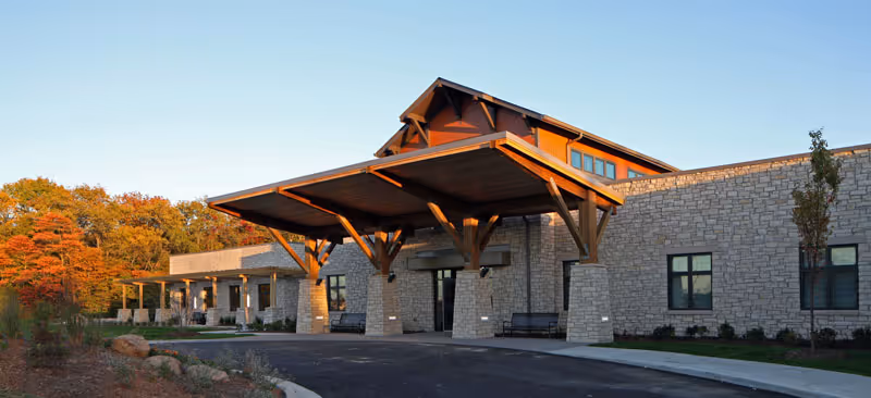 Stone exterior of a senior living center with a large wooden porte-cochère entrance.