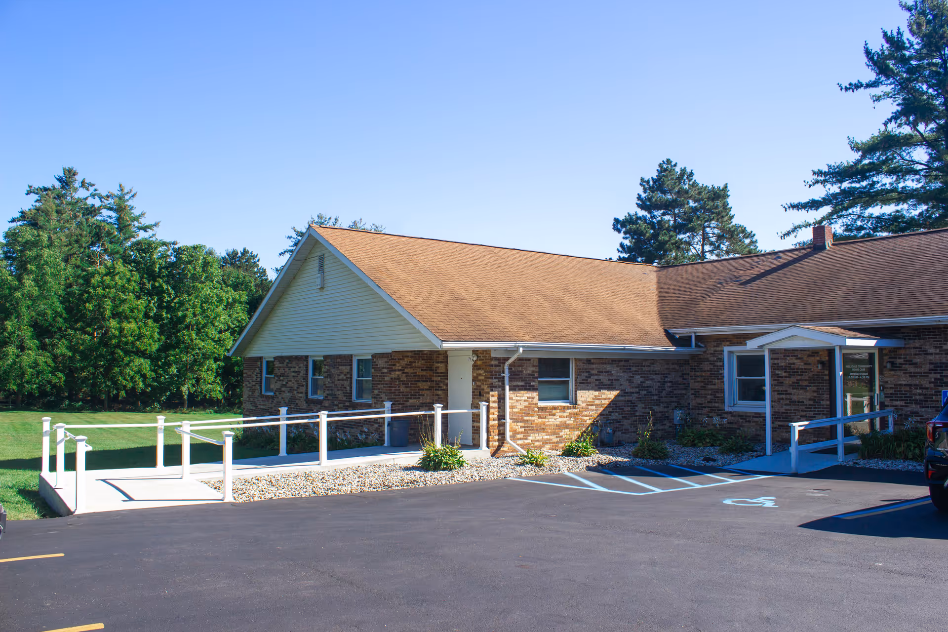 Exterior view of a single-story brick senior care facility with an accessible ramp and parking.