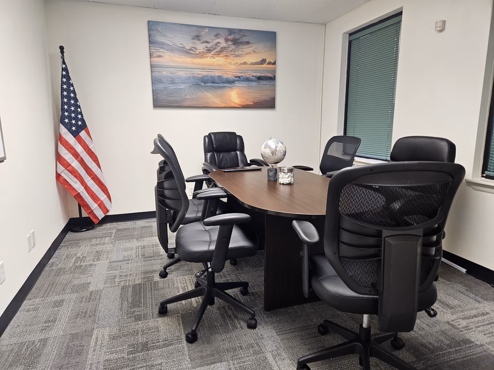 Conference room with a wooden table, black executive chairs, American flag, globe, and wall art.