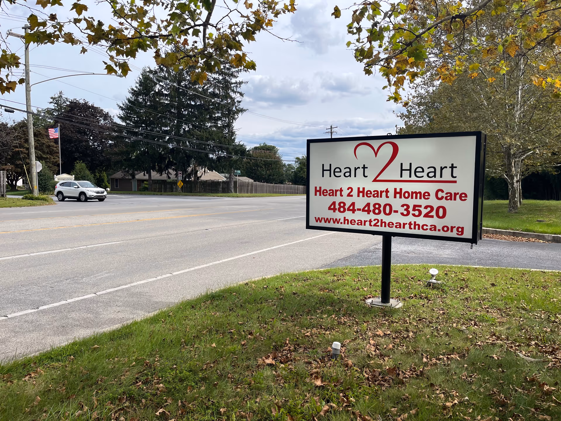 Roadside sign for Heart 2 Heart Home Care Agency on a grassy median beside a street.