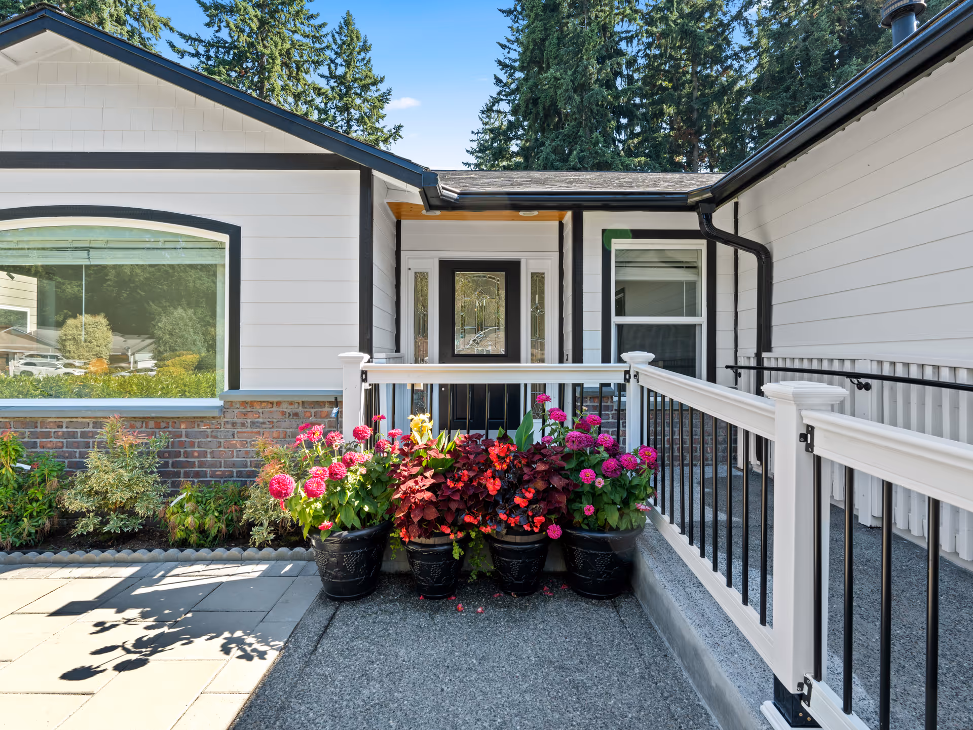 Exterior of a white senior living facility with a front entrance and colorful potted flowers.