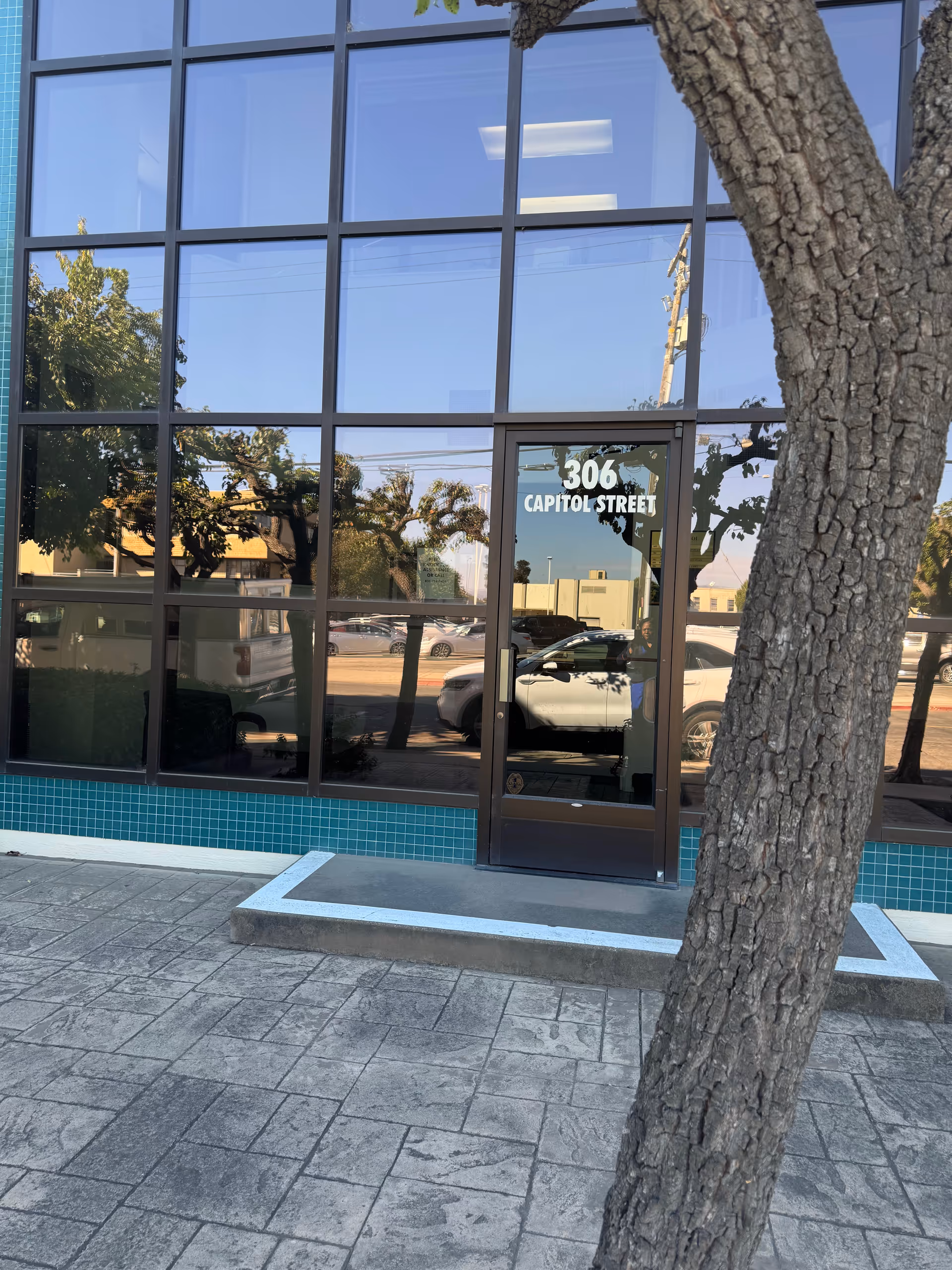 Glass storefront facade with entrance door labeled 306 Capitol Street, tree in foreground.