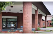 Brick building entrance with glass doors, large columns, and a landscaped entryway.