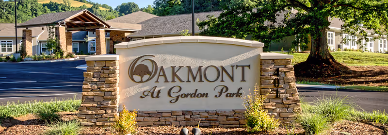 Oakmont at Gordon Park entrance sign with stone base, driveway, and building in the background.