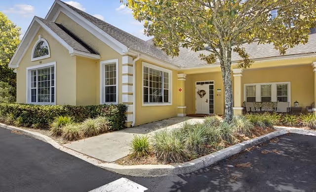 Yellow single-story senior living facility exterior with front entrance and porch seating.