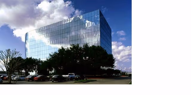 Glass office building with sky reflections, surrounded by trees and a parking lot.
