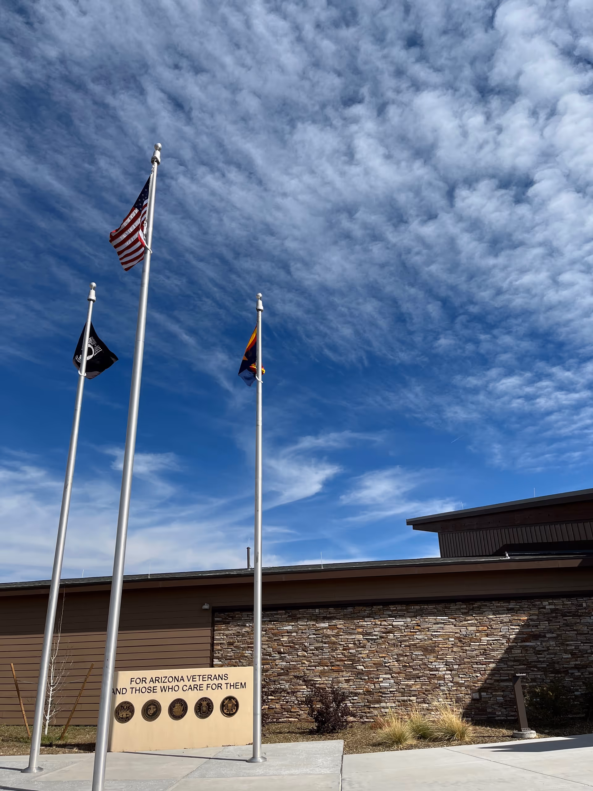 Three flagpoles with flags stand in front of the Flagstaff Arizona State Veteran Home entrance.
