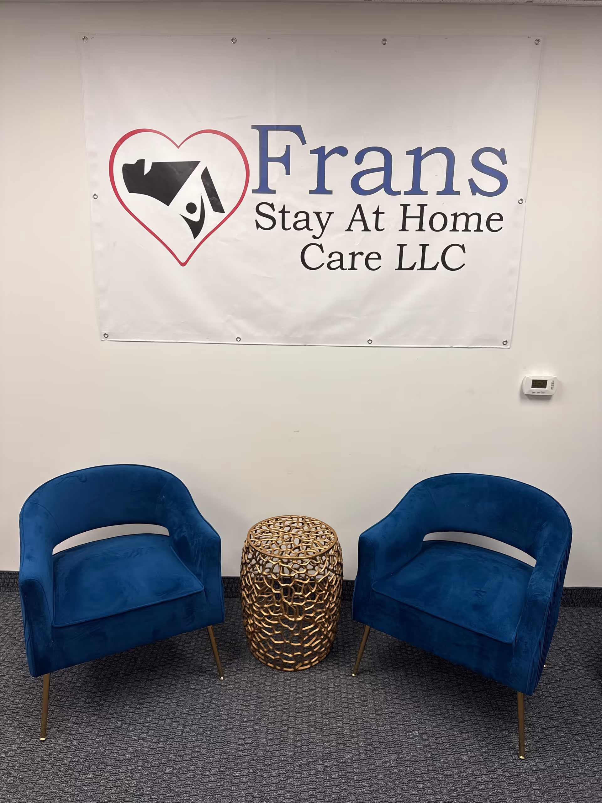 Two blue armchairs with metal side table sit beneath a Frans Stay At Home Care banner.
