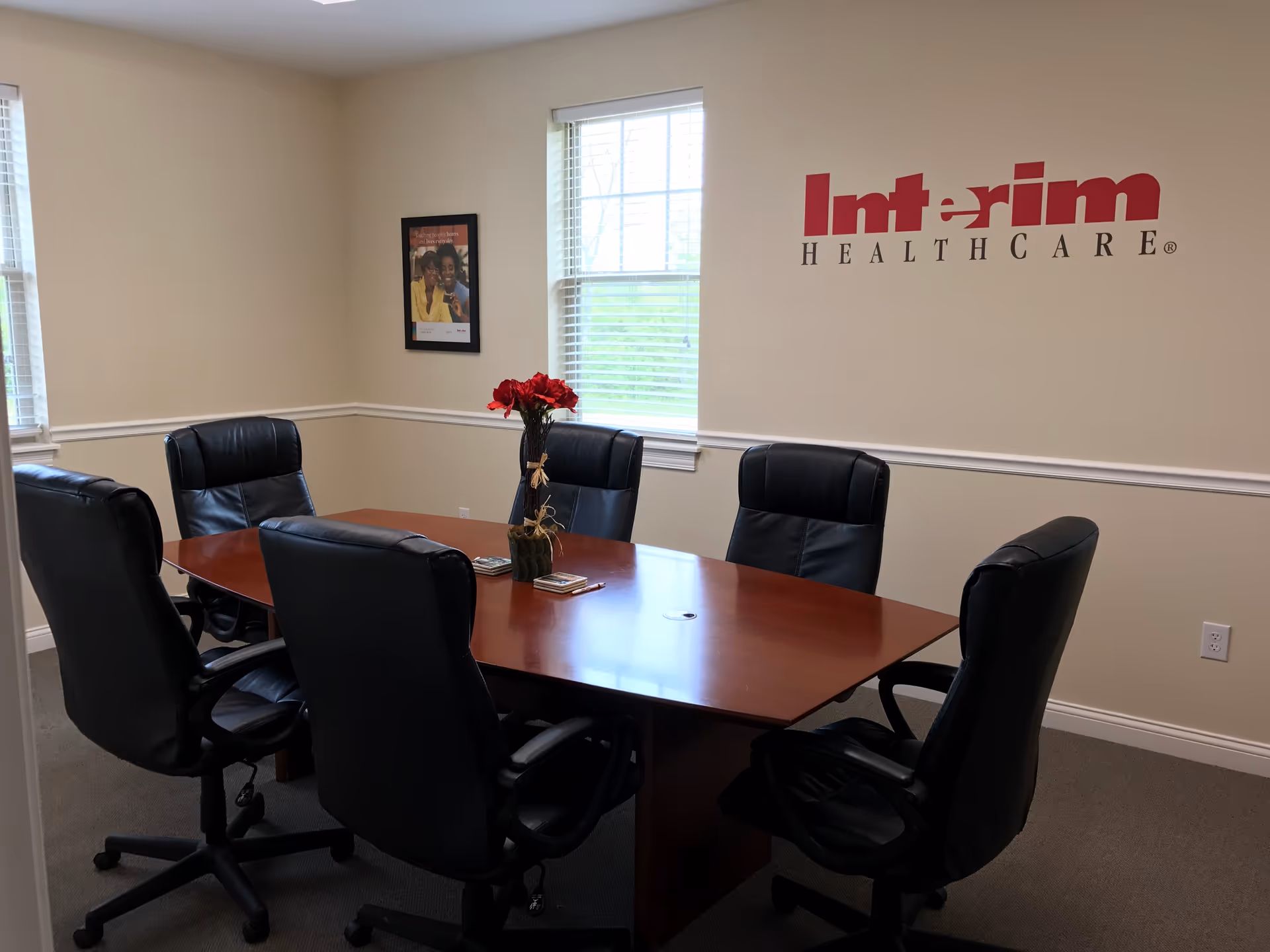 A conference room with a wooden table, black chairs, and an Interim HEALTHCARE sign.