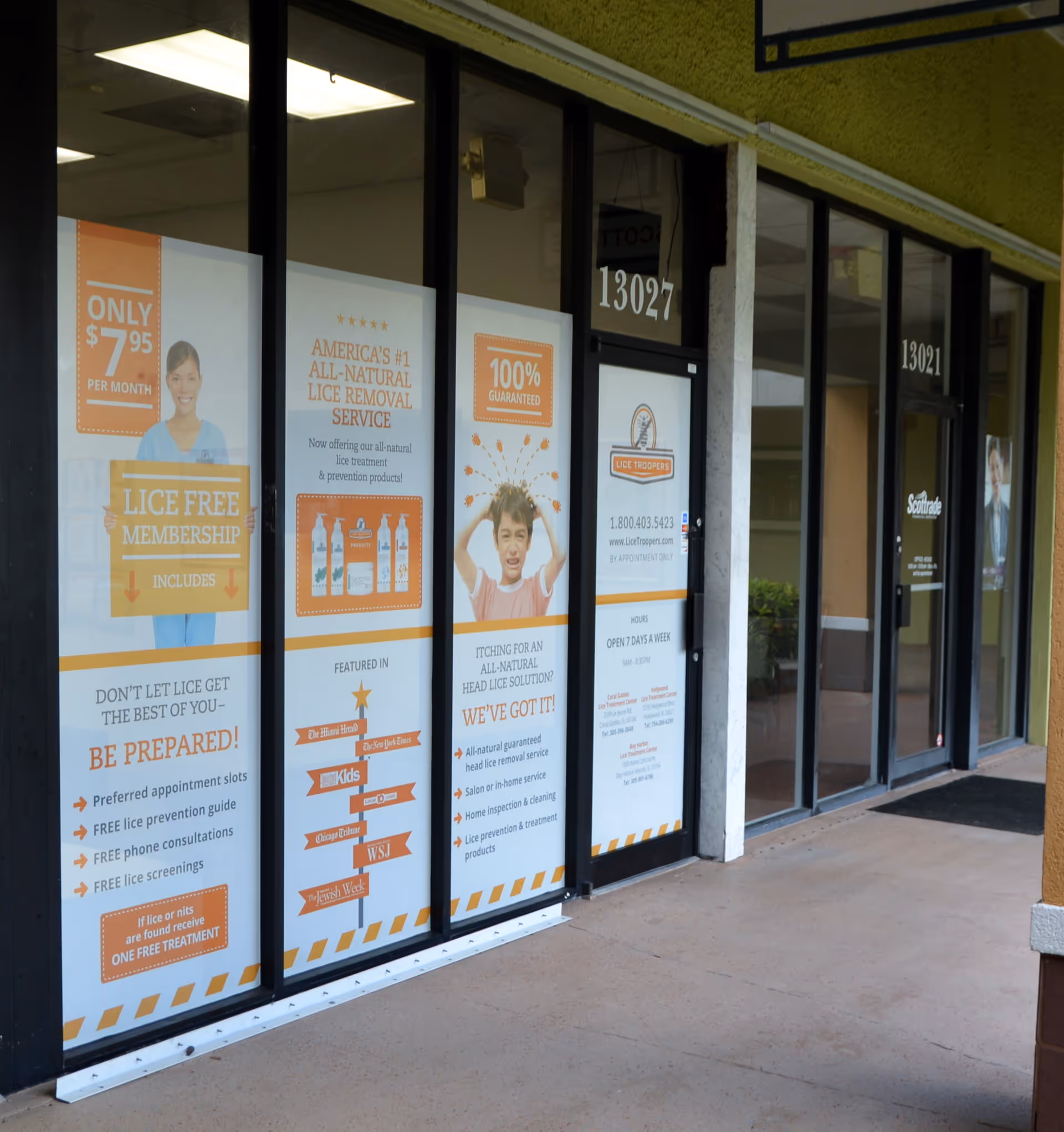 A storefront with orange posters advertising lice removal on glass windows.