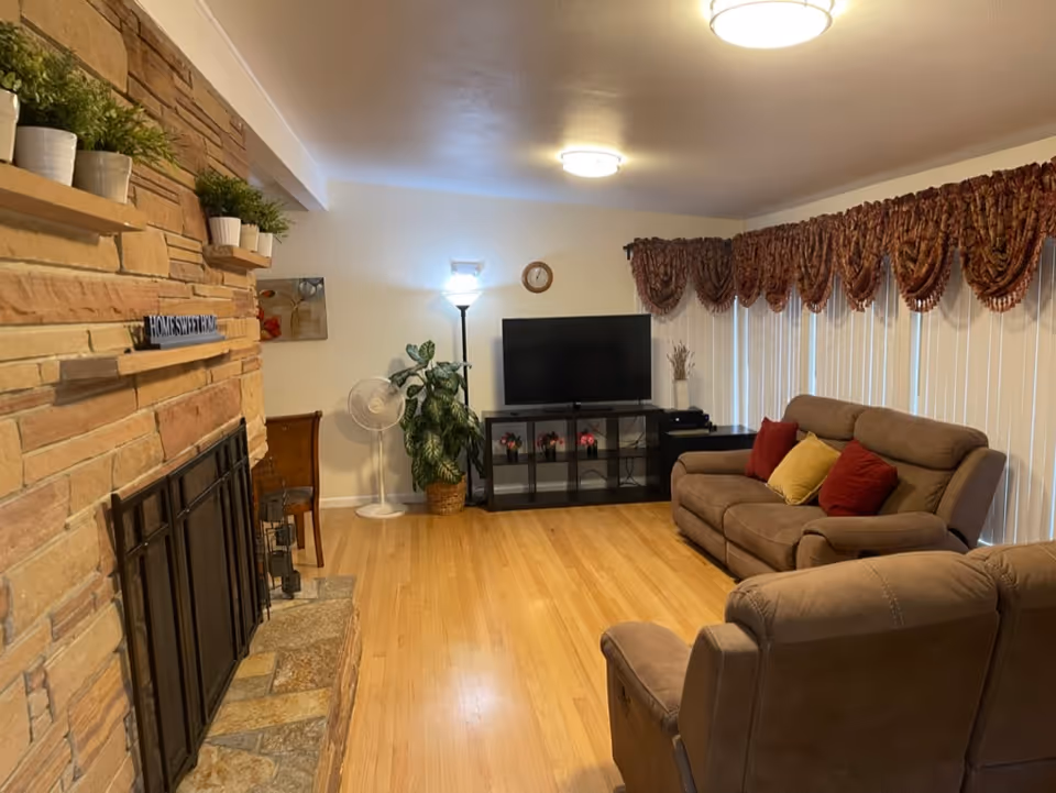 Cozy living room with a stone fireplace, comfortable sofas, TV, and decorative plants.