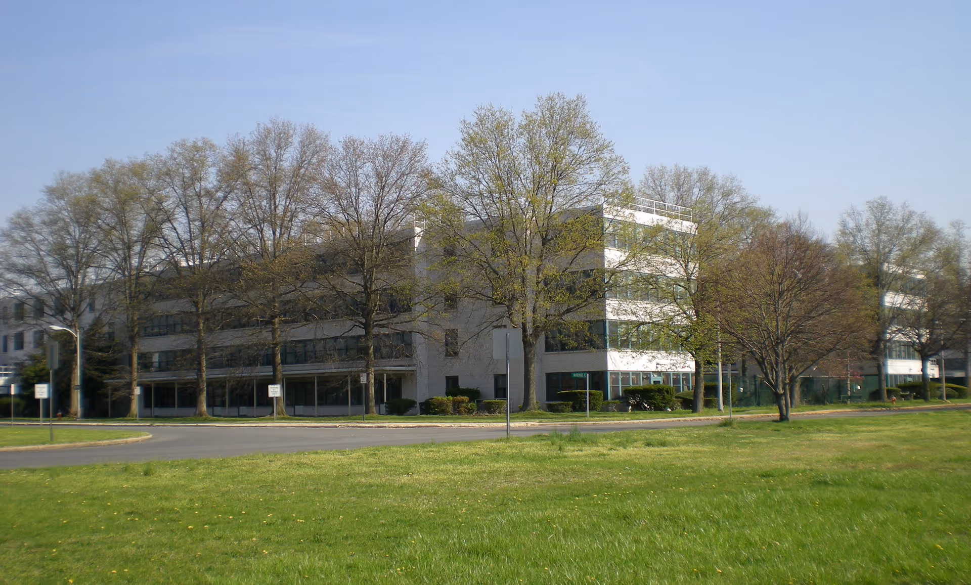 Exterior of a modern, multi-story senior care facility with trees and a grassy lawn.