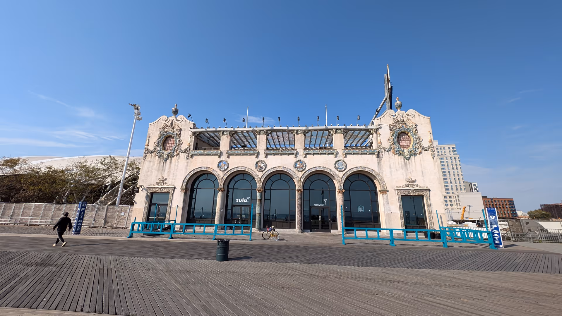 Exterior view of a decorative arched façade building with glass doors along a wooden boardwalk.