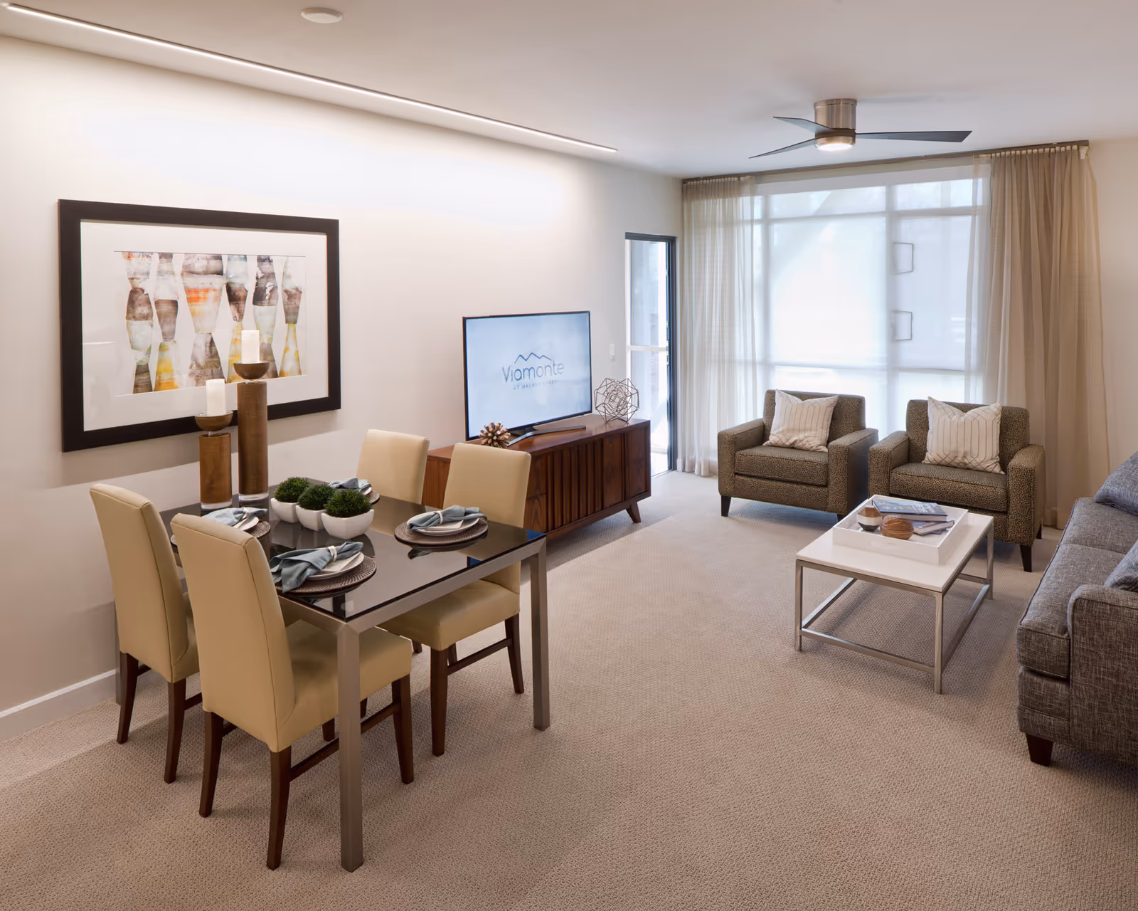 Bright modern combined living and dining area with a dining table, TV on a console, armchairs, a sofa, and a large window with sheer curtains.