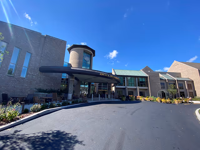 Exterior view of a brick senior living facility with a curved entrance canopy and parking.