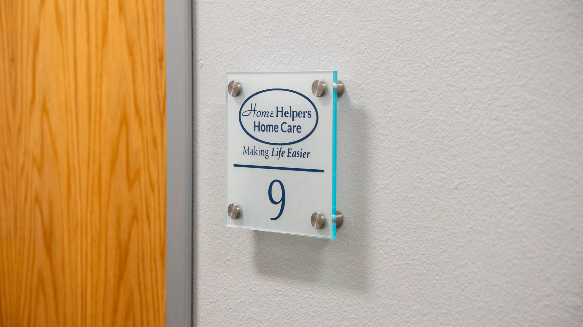 Glass plaque displaying Home Helpers Home Care logo and the number 9 on a wall.