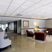 Bright lobby area with seating, a lamp, and a hallway at the back.