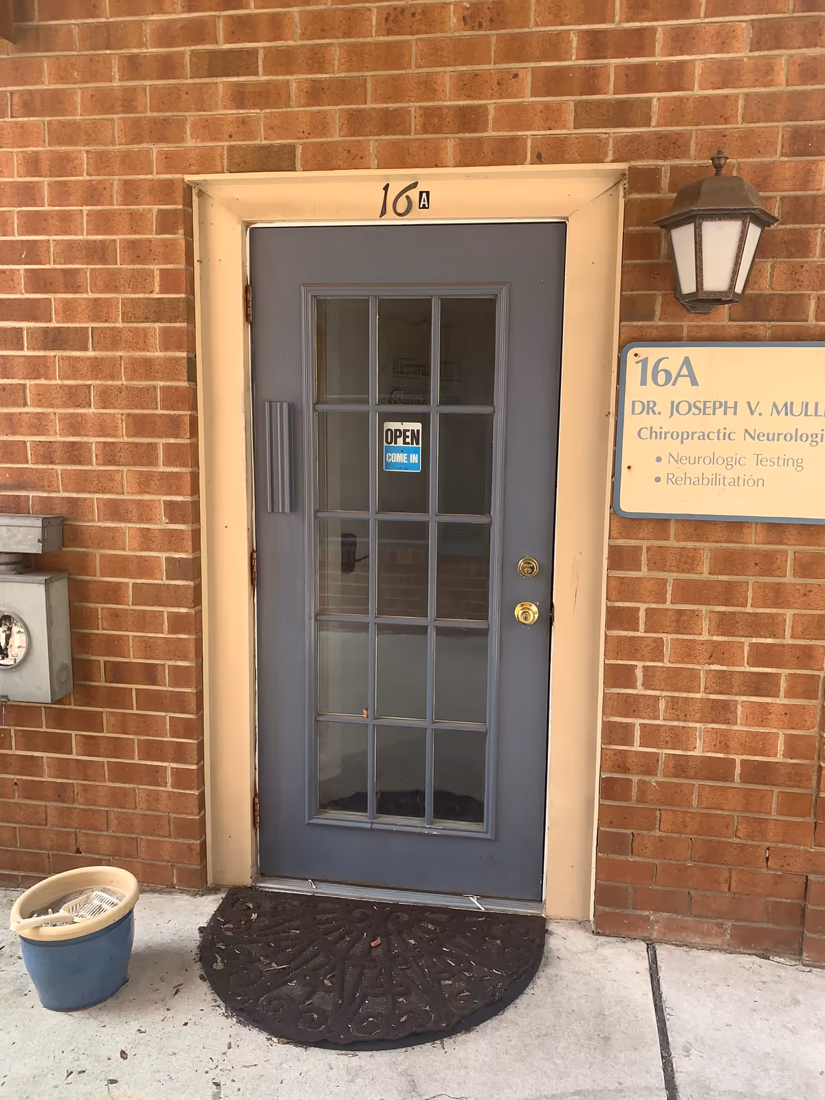 Brick exterior with a blue glass-paneled door labeled 16A and an open sign on concrete doorstep.