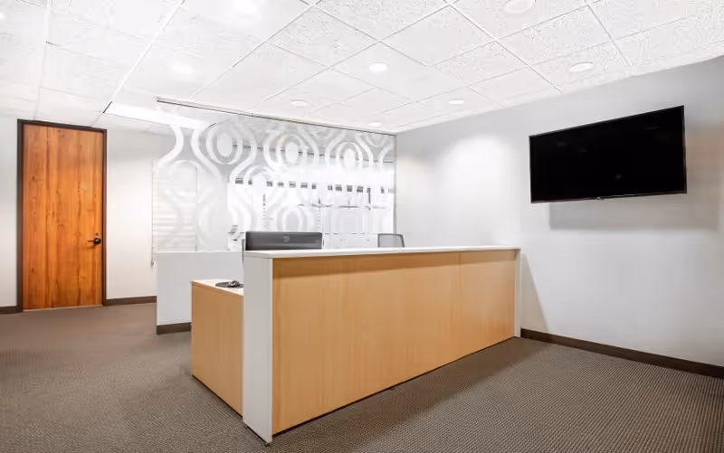Reception desk in a modern, quiet lobby with patterned wall and wall-mounted TV.