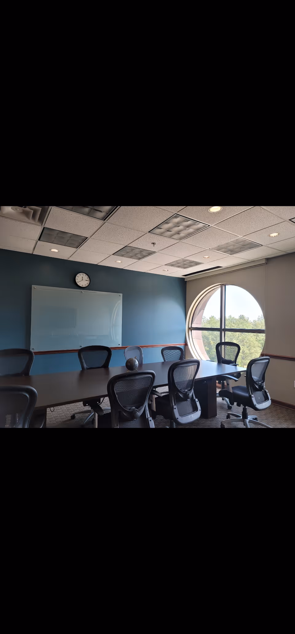 Interior conference room with long table, chairs, whiteboard, clock, and round window.