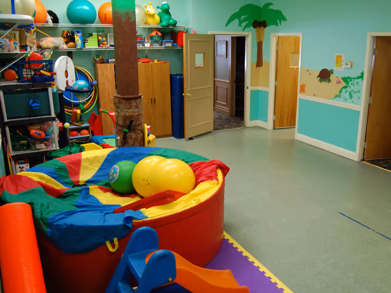 Bright pediatric therapy room filled with colorful toys, mats, and play equipment.