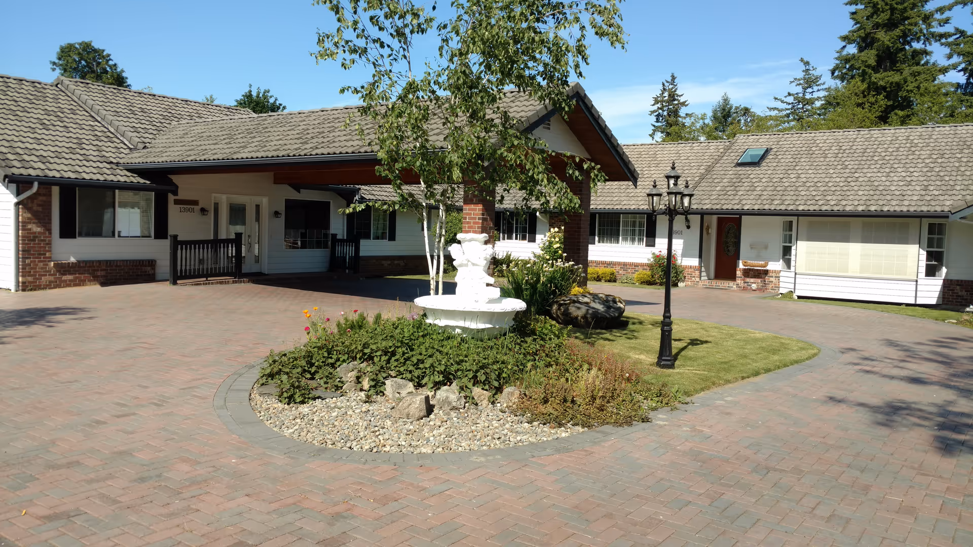 Exterior view of Country Living Adult Family Home with circular driveway, fountain, and landscaped island.