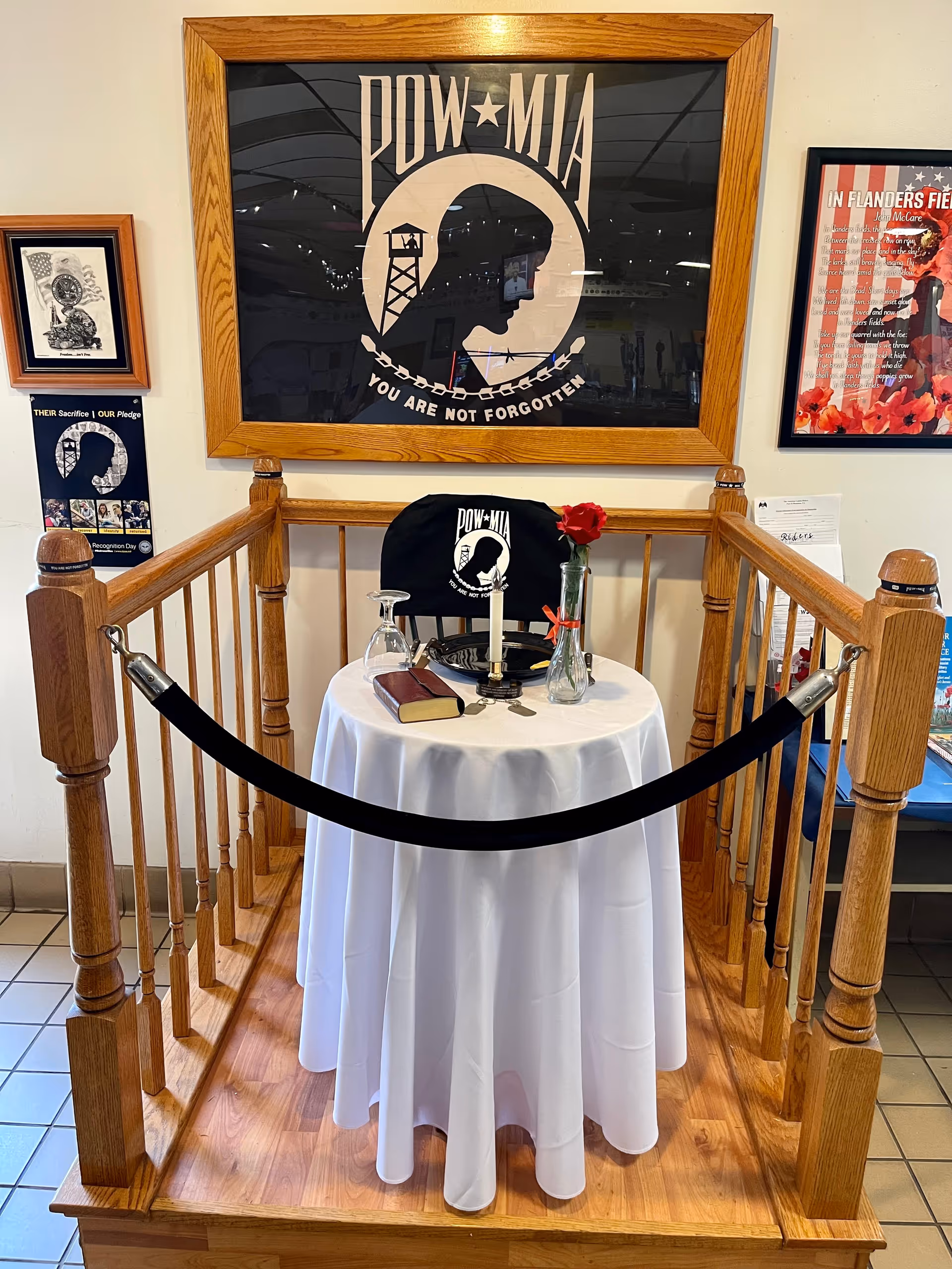 Small round table with white cloth, rose, candle, and POW-MIA display behind railing.