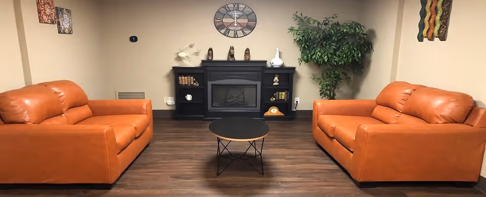 Small lounge with two orange leather sofas facing a round coffee table and a decorative fireplace console.