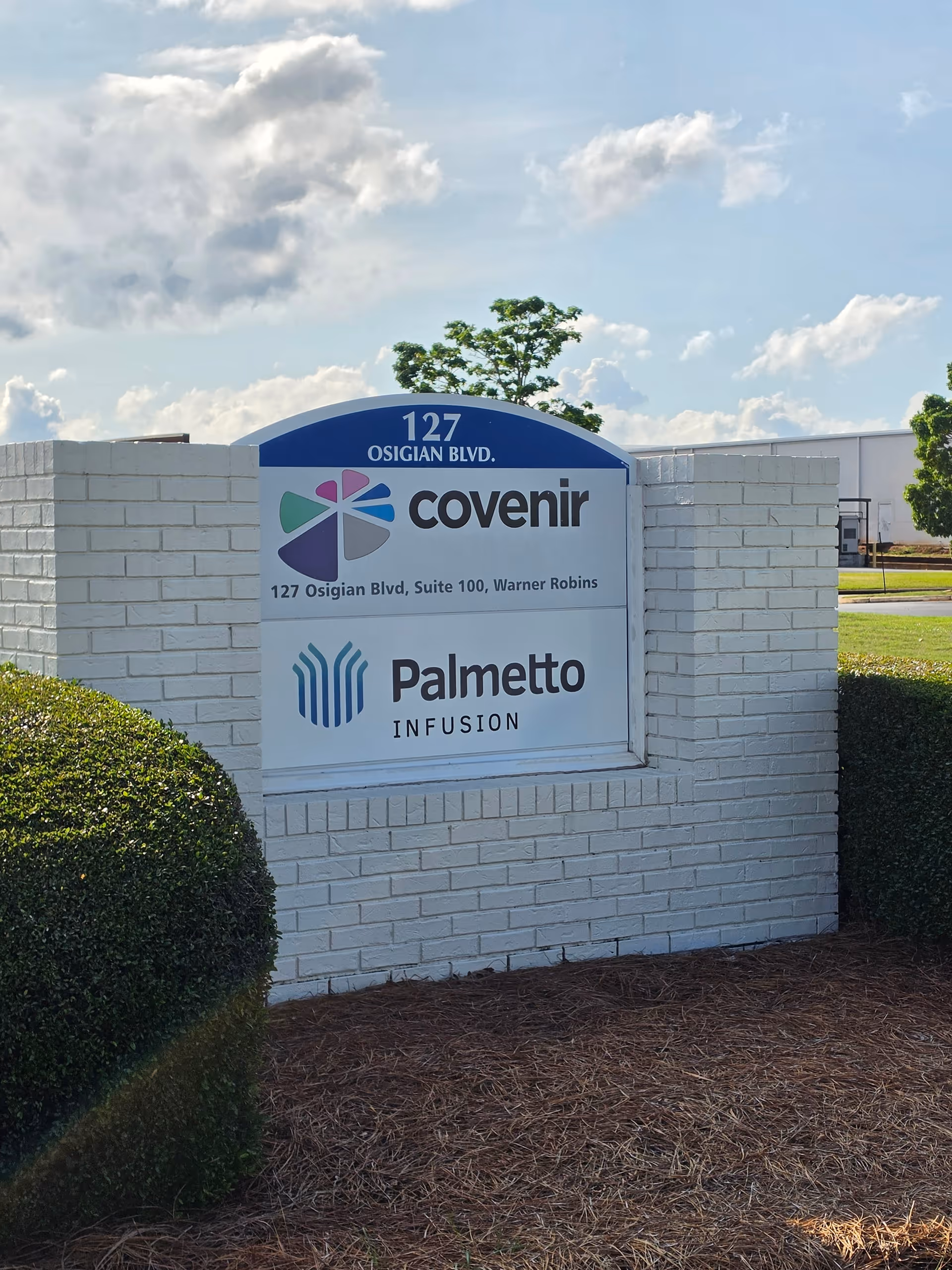 Exterior sign with Covenir and Palmetto Infusion logos on a white brick monument.