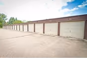 Row of brown garage doors along a paved exterior wall under a blue sky.