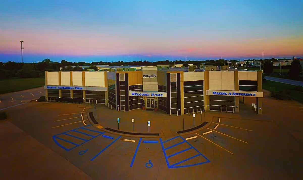 A modern senior living facility with beige exterior, glass entry, and blue parking lines.