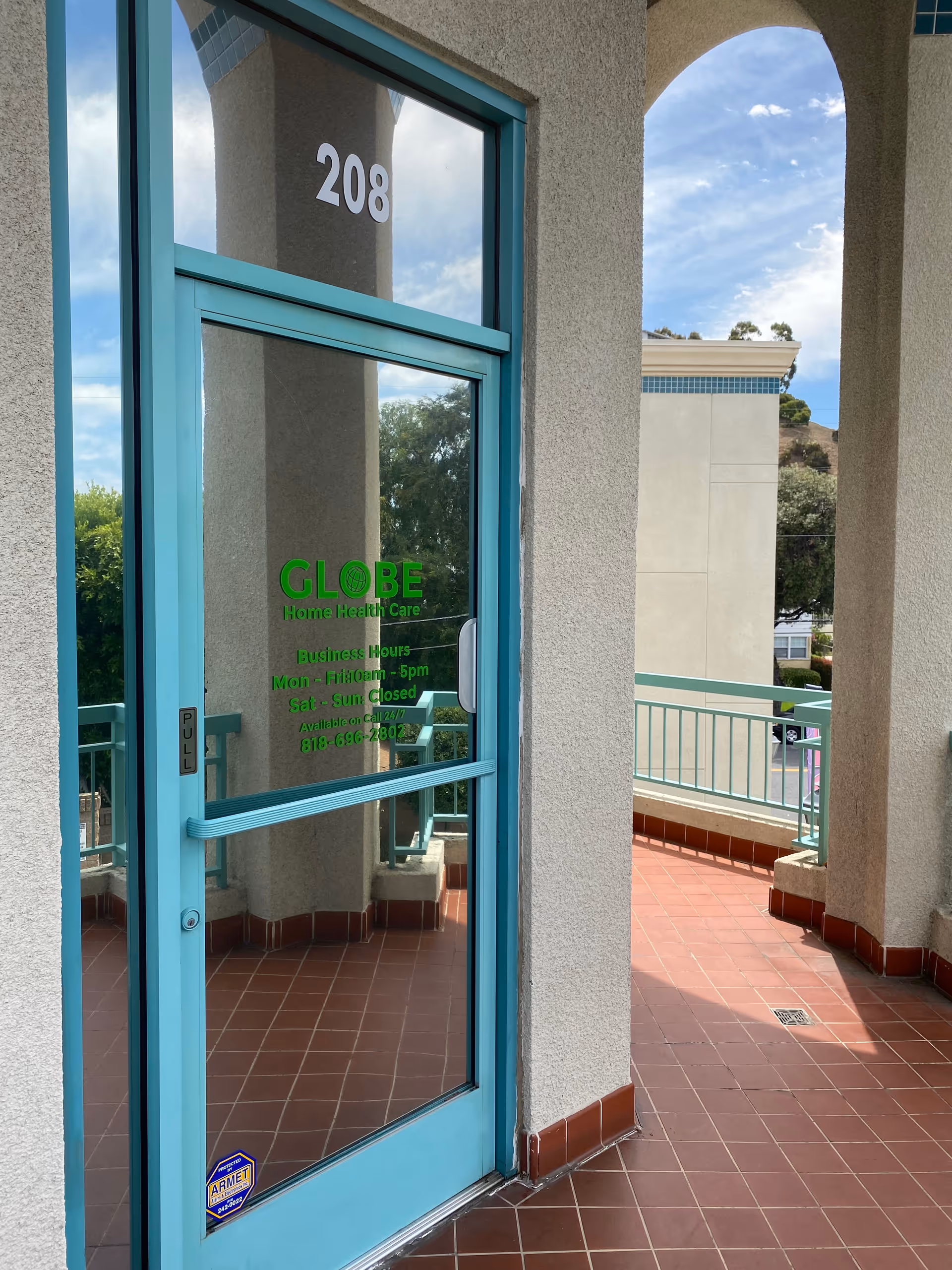 Turquoise-framed glass door with Globe Home Health Care sign beside building entrance, 208 on the wall