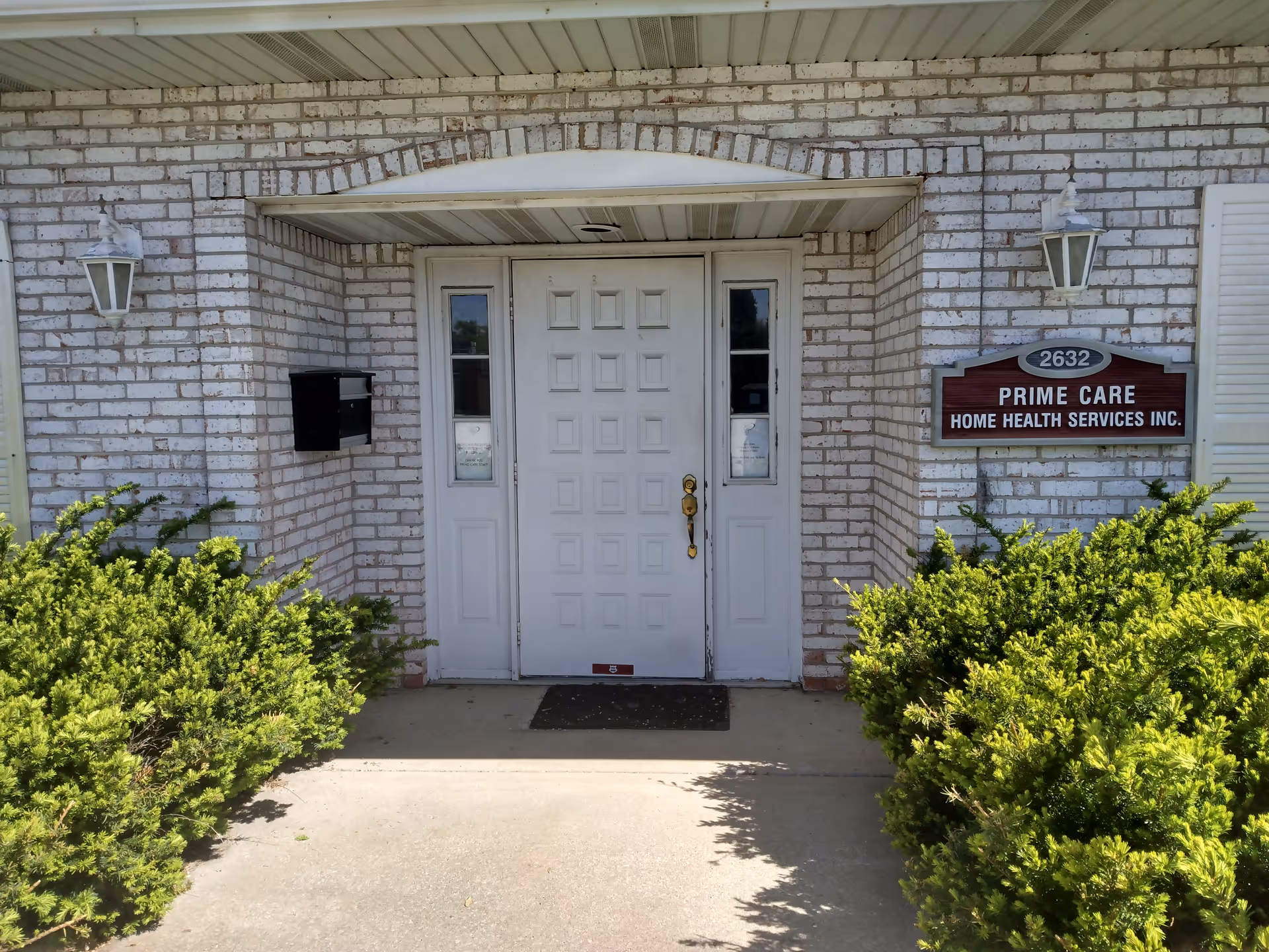 Brick exterior entrance with double doors and a Prime Care sign, shrubs lining the walkway.
