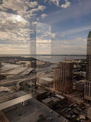 City skyline and waterfront viewed through a window, with reflections and tall buildings.