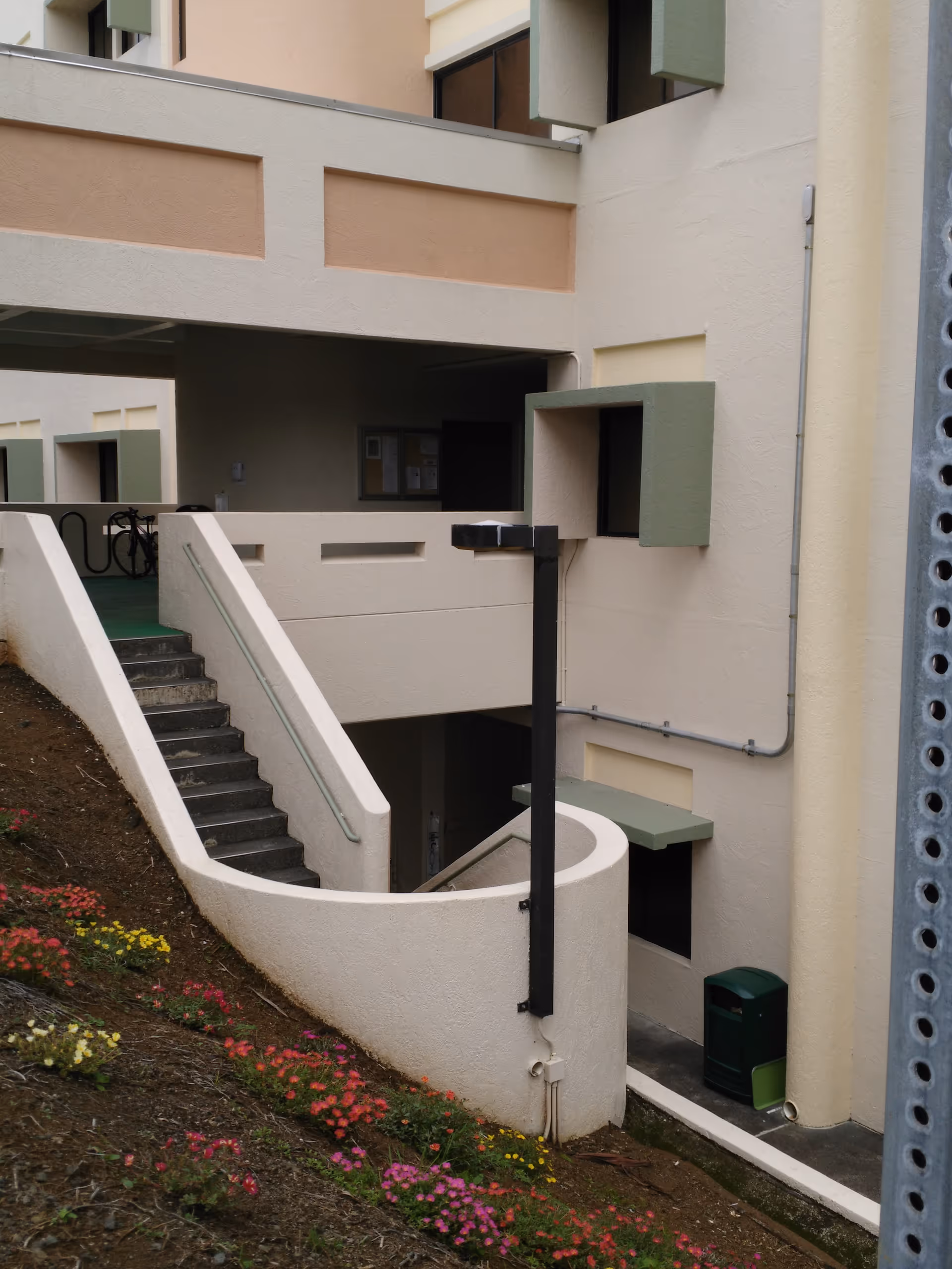 Exterior view of a beige multi-level building with stairs, ramp, and flowered landscaping.