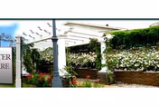 Covered walkway with white columns, flowering planters along a brick wall near entrance.