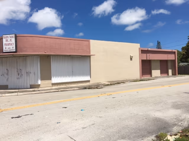 Exterior view of a beige building with pink trim and closed storefront shutters along a street.