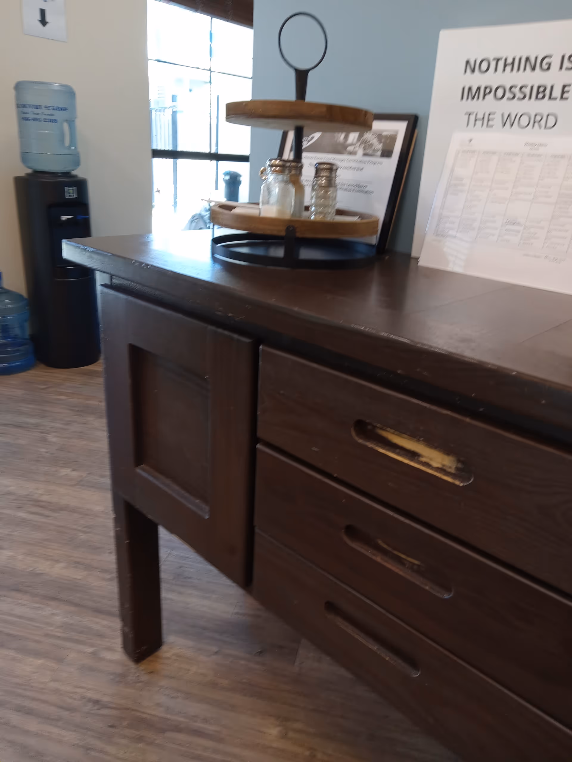 Dark wooden reception counter with a two-tier tray, salt shakers, and a nearby informational sign.