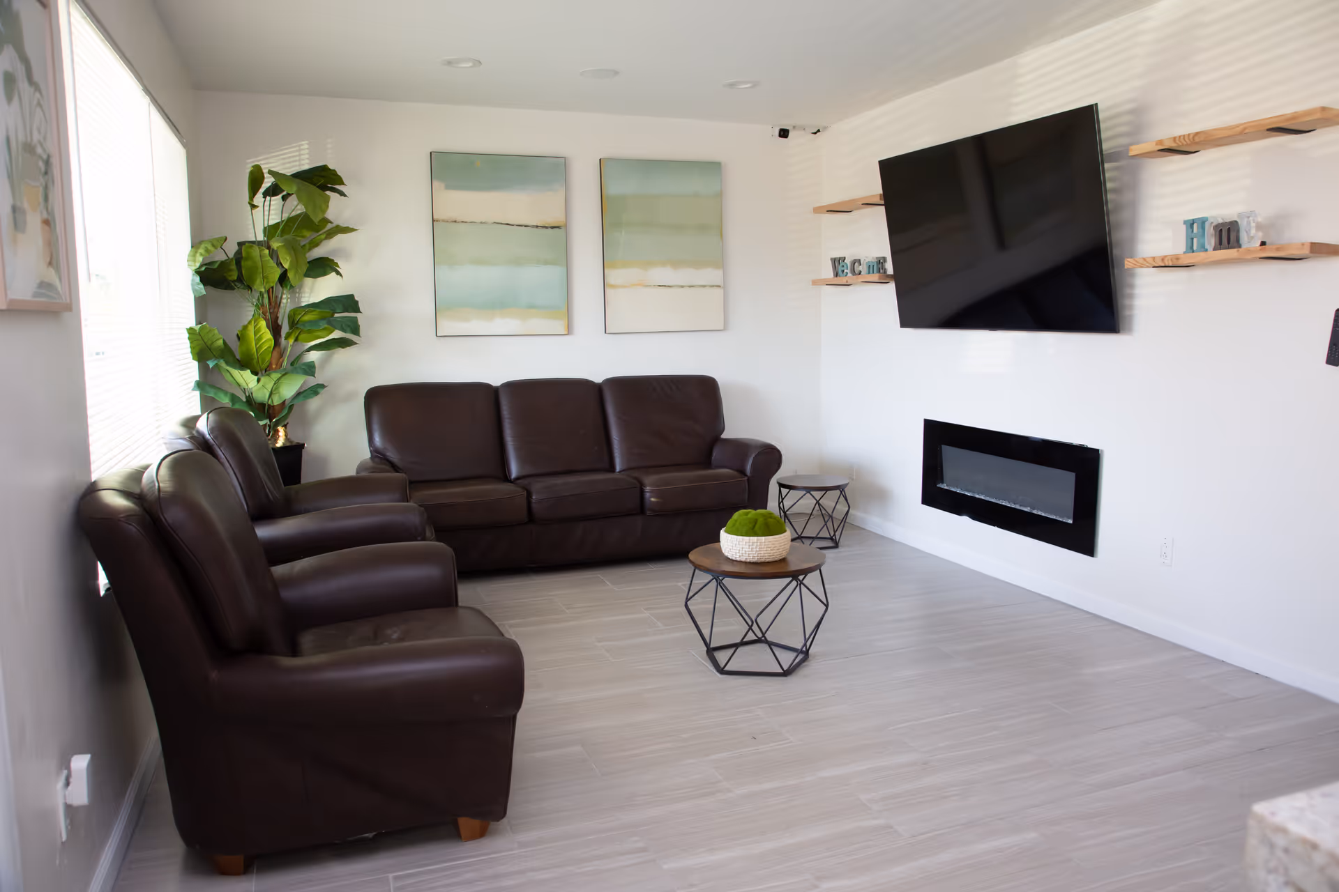 Modern senior living lounge featuring brown leather seating, wall-mounted TV, shelves, and fireplace.