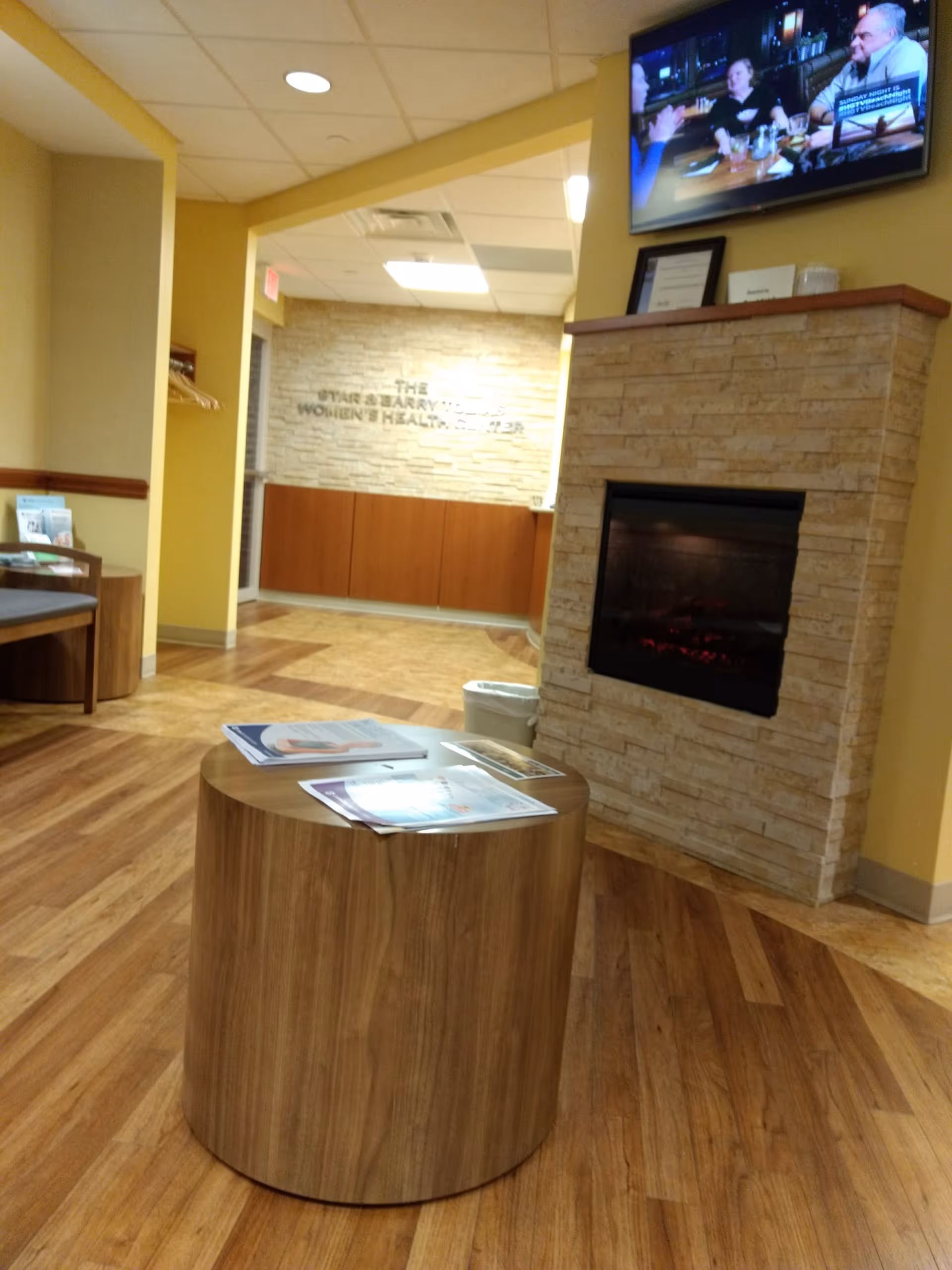 Lobby waiting area of Women's Health Center at CentraState with fireplace, TV, and round coffee table.