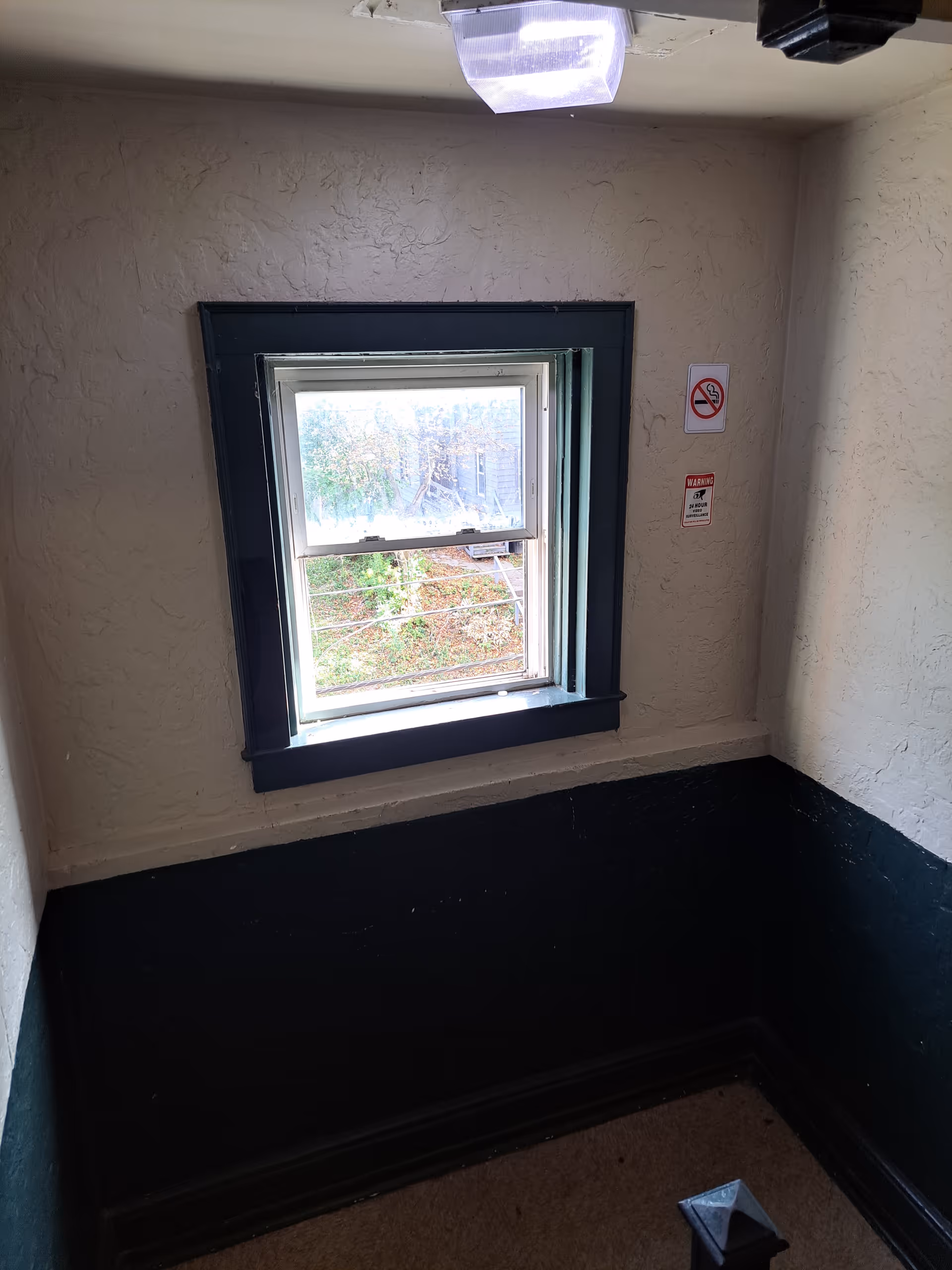 Interior stairwell corner with a small window, textured walls, and dim overhead light.