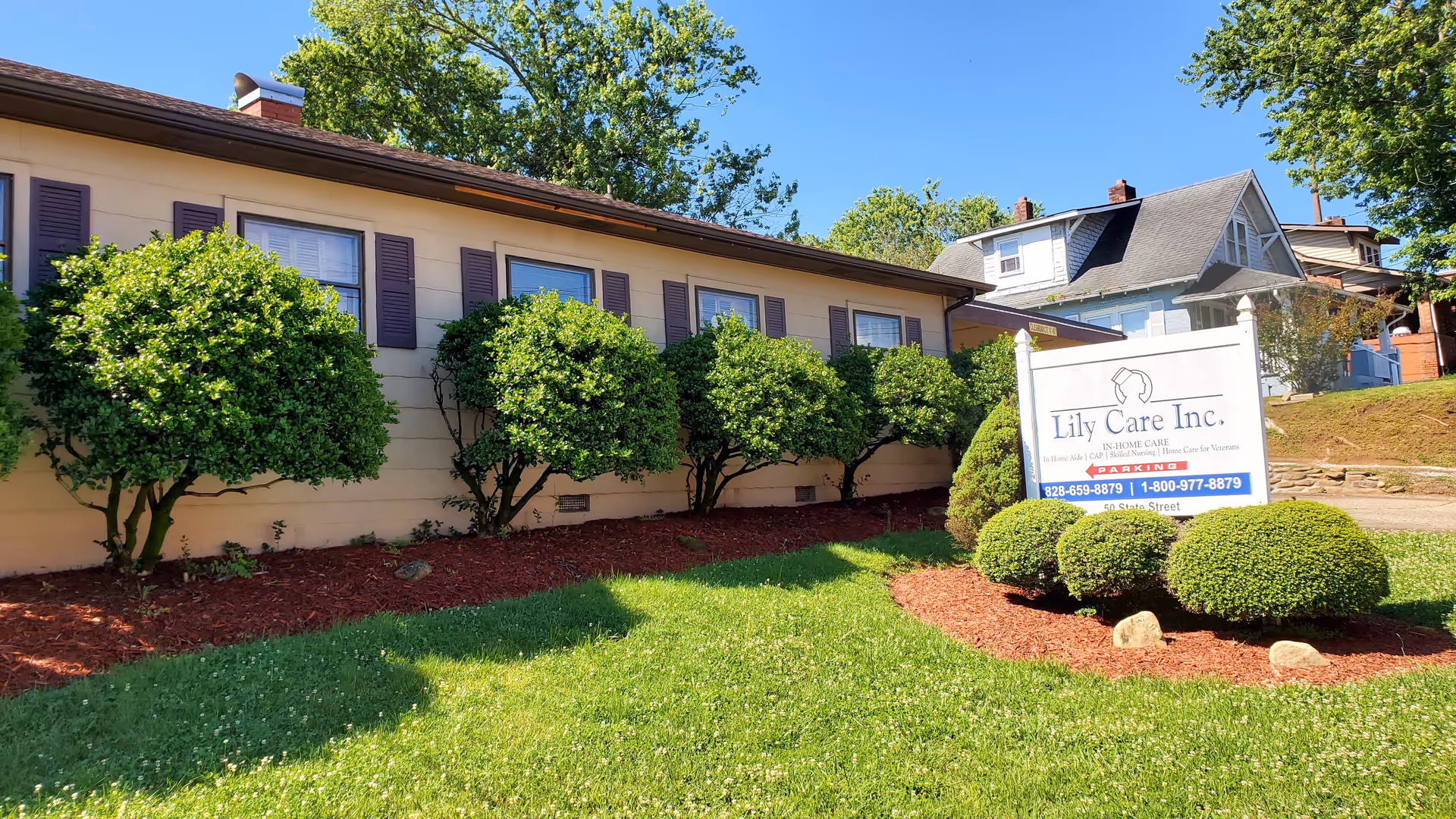 Exterior view of Lily Care facility with a sign, shrubs, and a green lawn.