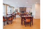 Sunlit dining room with wooden tables, chairs, and a central fireplace.
