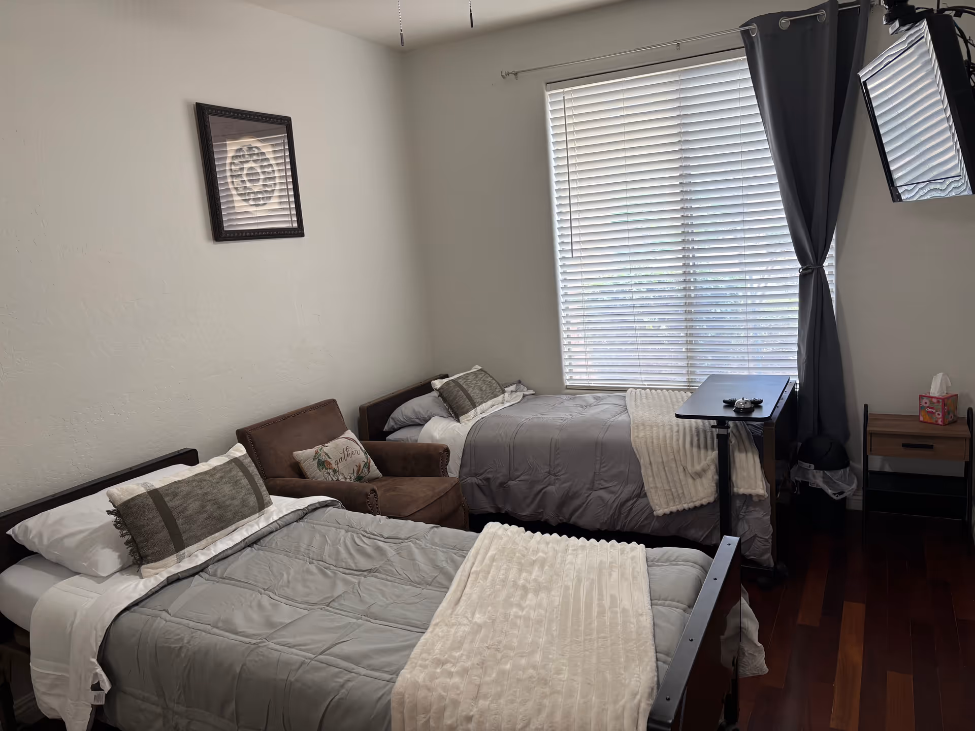 Two single beds with gray bedding in a shared bedroom near a window with blinds.