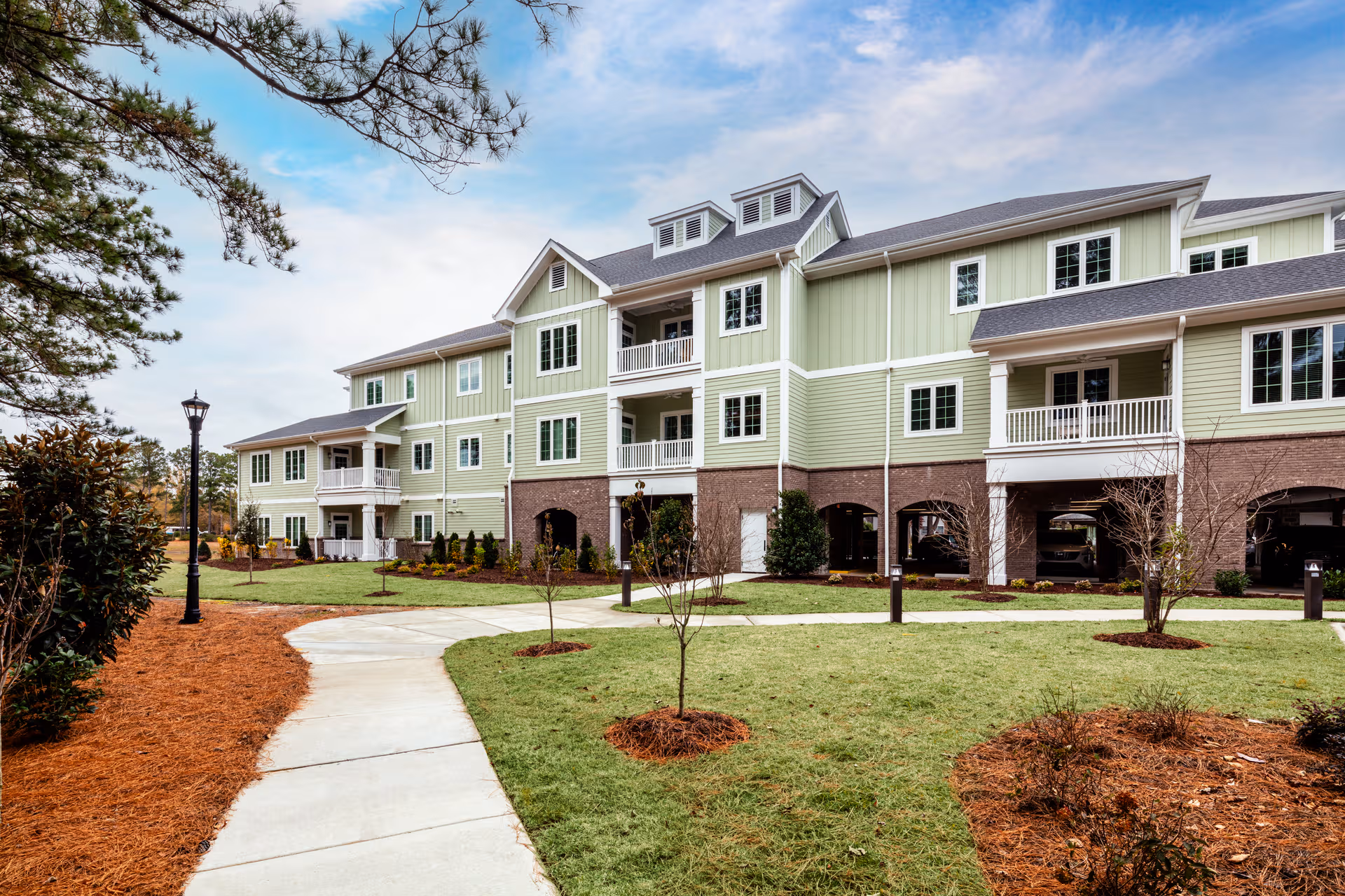 A green, multi-story senior living building with brick base and landscaped lawn.