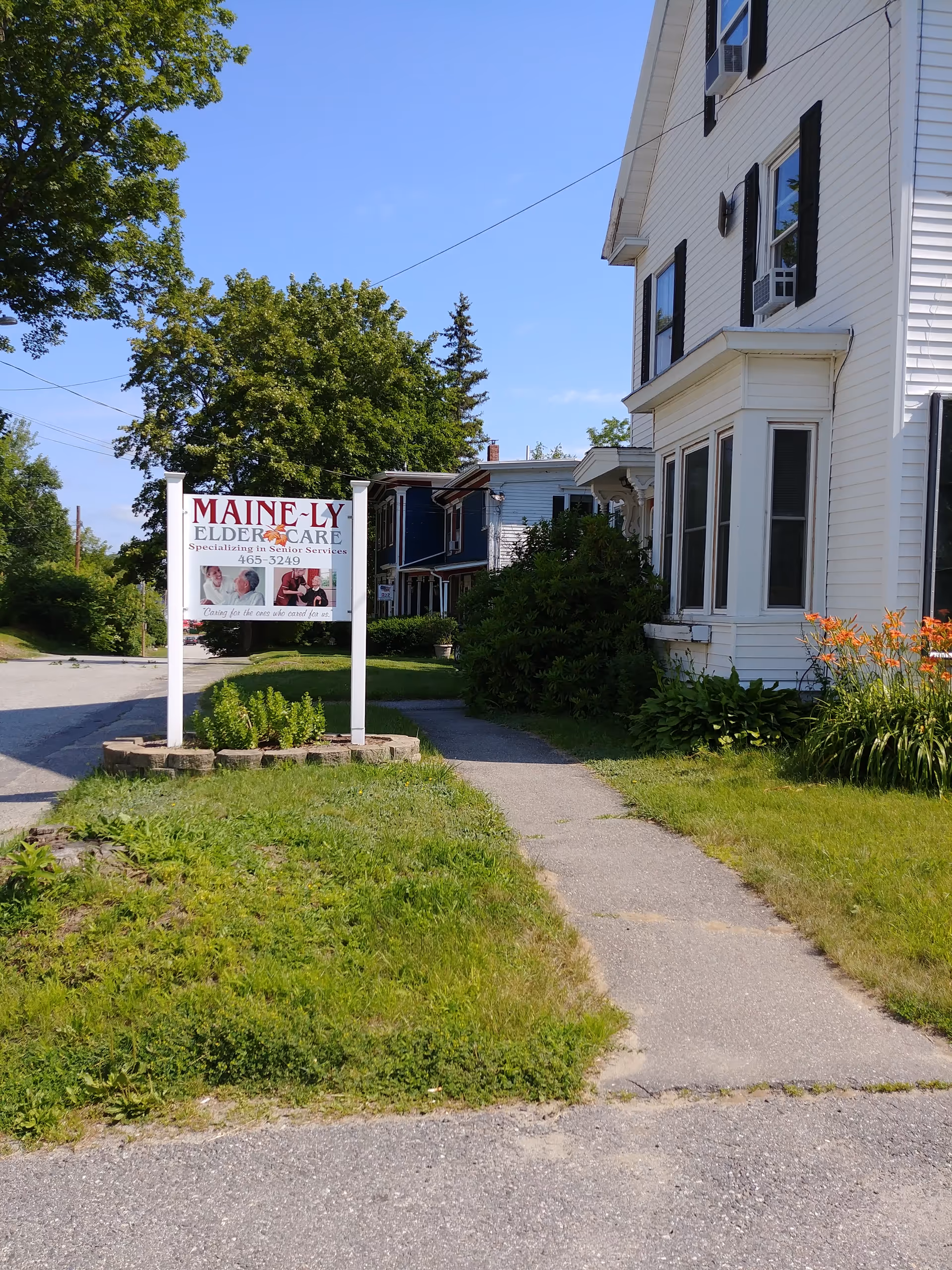 White two-story building with a Maine-ly Elder Care sign at the front yard.